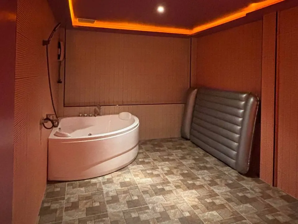A jacuzzi room at OHO777 on Sukhumvit Soi 33, Bangkok: corner tub, shower and an inflatable nuru mattress under amber lighting