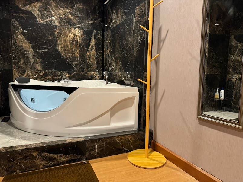 曼谷素坤逸20巷 EXOTIC Massage Bangkok 的按摩浴缸：深色大理石牆前的白色轉角浴缸，旁邊立著木製衣架